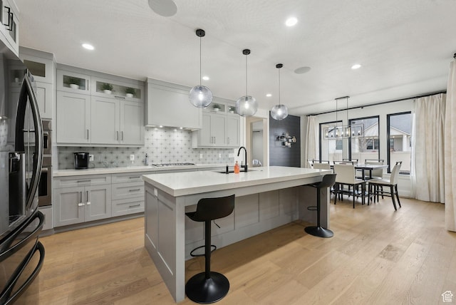kitchen with light wood-style flooring, premium range hood, gas stovetop, a kitchen breakfast bar, and light countertops