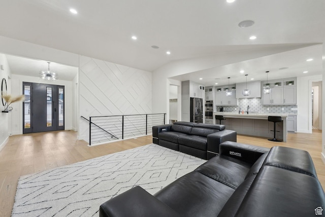 living area with light wood finished floors, baseboards, lofted ceiling, a chandelier, and recessed lighting