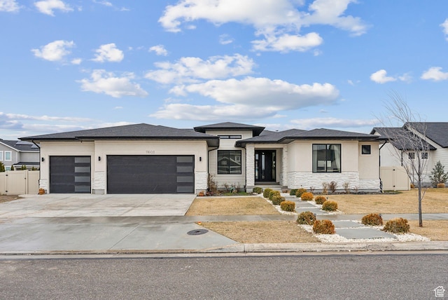 prairie-style home featuring a garage, fence, stone siding, concrete driveway, and stucco siding