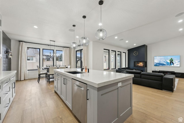kitchen with stainless steel dishwasher, light wood-type flooring, a sink, and a center island with sink