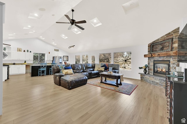 living room featuring light wood-type flooring, a fireplace, high vaulted ceiling, and a ceiling fan