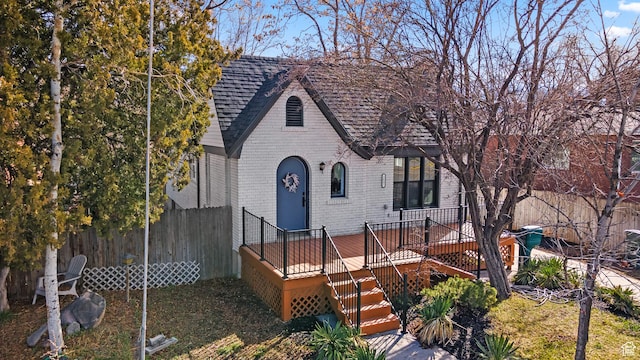 english style home featuring stairway, roof with shingles, fence, a deck, and brick siding