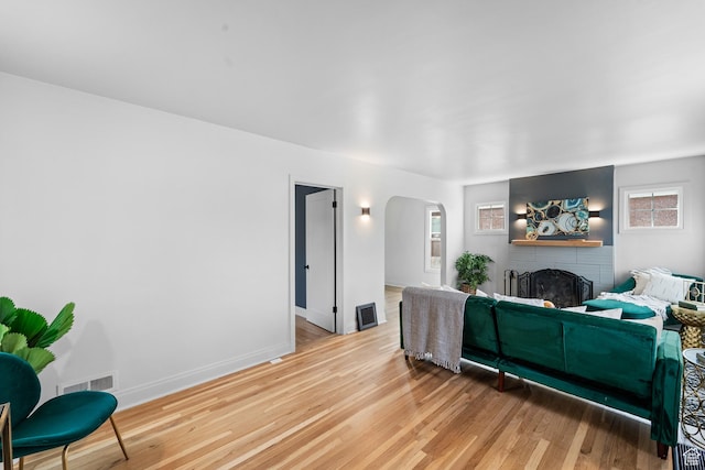 living area featuring arched walkways, visible vents, light wood-style flooring, a brick fireplace, and baseboards