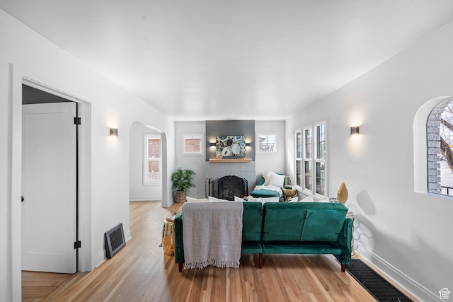 living area with baseboards, visible vents, arched walkways, light wood-style floors, and a fireplace