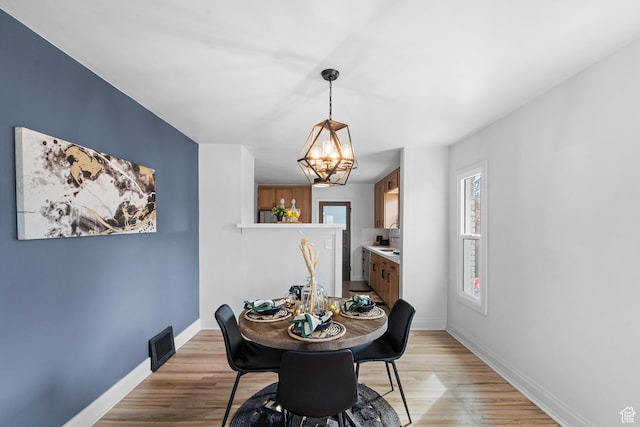 dining area with light wood-type flooring, baseboards, and a chandelier