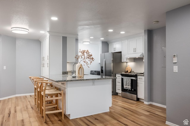 kitchen with gas range, under cabinet range hood, a peninsula, white cabinetry, and a breakfast bar