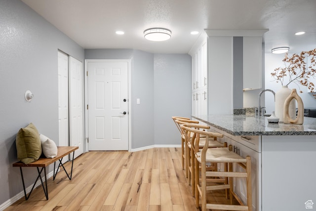 kitchen featuring white cabinets, baseboards, light wood-type flooring, stone counters, and a kitchen bar