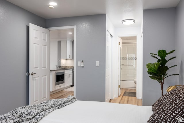 bedroom with light wood-style flooring, a sink, and ensuite bath