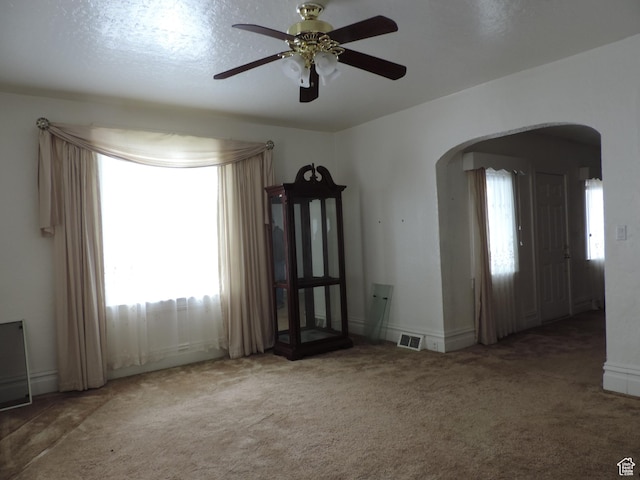 carpeted spare room with arched walkways, visible vents, and a ceiling fan