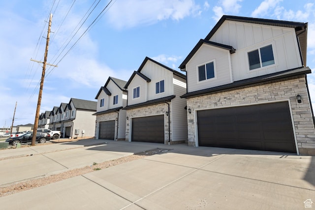 view of front of home featuring concrete driveway, board and batten siding, a garage, a residential view, and stone siding