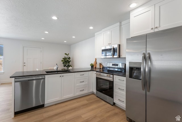 kitchen with light wood finished floors, stainless steel appliances, white cabinetry, a sink, and a peninsula