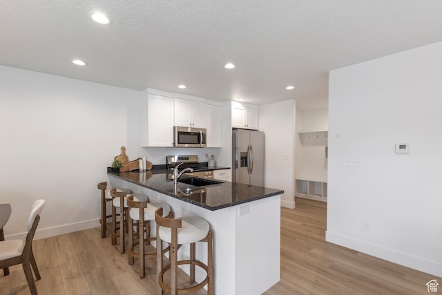 kitchen with a breakfast bar area, light wood-style flooring, appliances with stainless steel finishes, a sink, and a peninsula