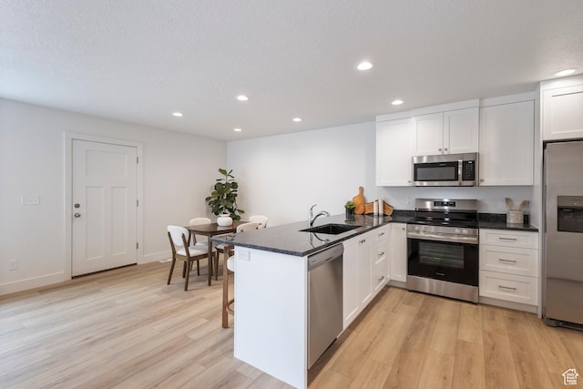 kitchen with a peninsula, a sink, white cabinets, appliances with stainless steel finishes, and light wood finished floors