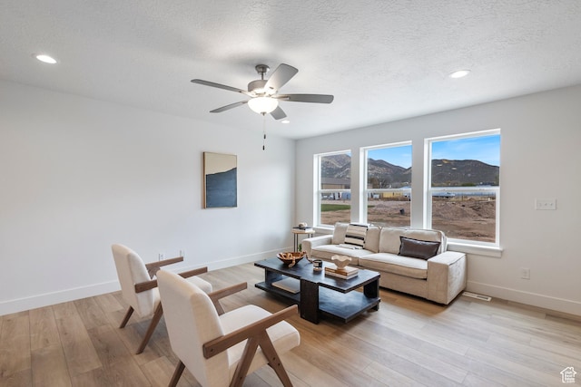living area featuring a textured ceiling, light wood finished floors, recessed lighting, and baseboards