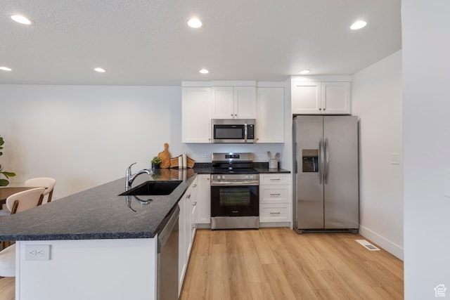 kitchen featuring light wood-style flooring, stainless steel appliances, a peninsula, a sink, and white cabinets