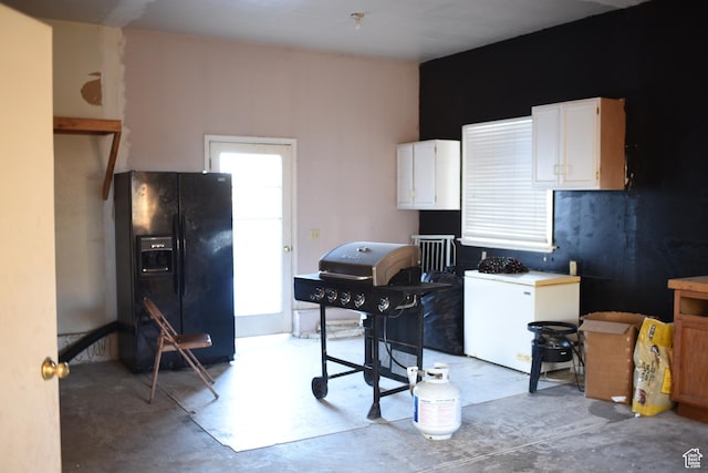 kitchen with white cabinetry, black refrigerator with ice dispenser, unfinished concrete flooring, and refrigerator