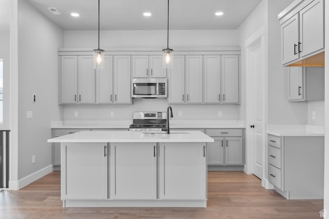 kitchen featuring stainless steel appliances, light countertops, a sink, and light wood finished floors