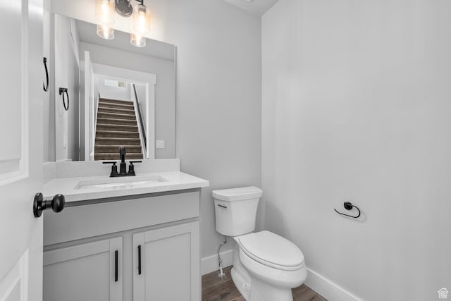 half bath featuring visible vents, toilet, vanity, wood finished floors, and baseboards