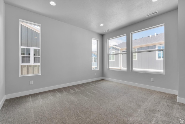 carpeted spare room with a healthy amount of sunlight, baseboards, visible vents, and a textured ceiling