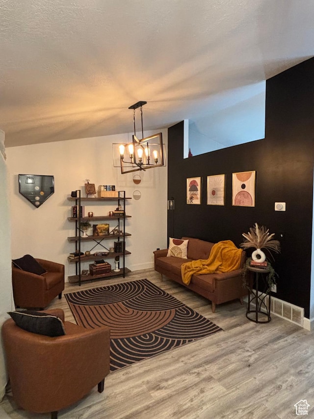 living room with a textured ceiling, a chandelier, wood finished floors, visible vents, and vaulted ceiling