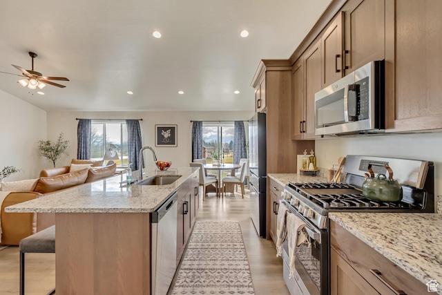 kitchen with an island with sink, a breakfast bar, open floor plan, stainless steel appliances, and a sink