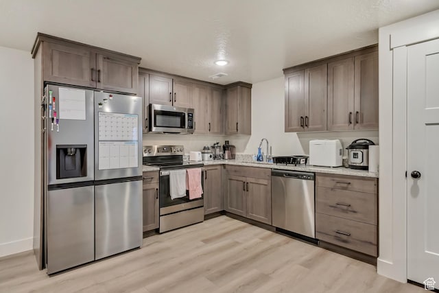 kitchen featuring stainless steel appliances, light wood-style floors, a sink, and light stone counters