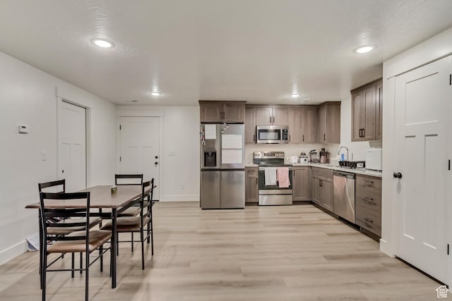 kitchen with appliances with stainless steel finishes, a sink, light wood-style flooring, and baseboards