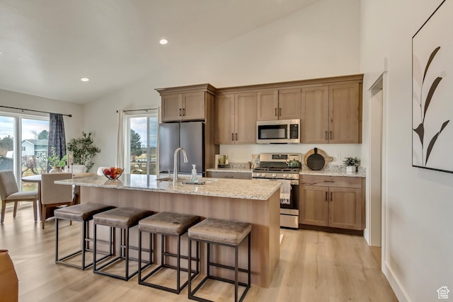 kitchen featuring appliances with stainless steel finishes, a sink, light stone counters, and a kitchen breakfast bar