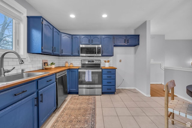 kitchen featuring appliances with stainless steel finishes, blue cabinets, a sink, and wooden counters