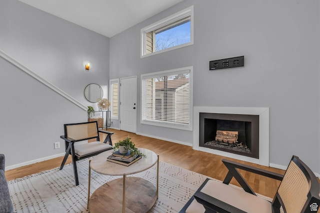 living area with a towering ceiling, a fireplace, baseboards, and wood finished floors