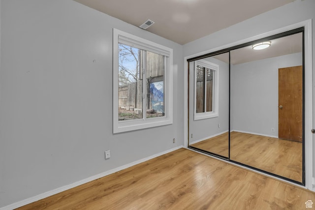 unfurnished bedroom with a closet, visible vents, baseboards, and wood finished floors