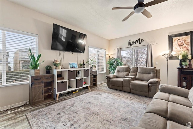 living area with ceiling fan, a textured ceiling, baseboards, and wood finished floors