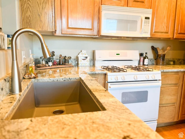 kitchen featuring light stone countertops, white appliances, and a sink