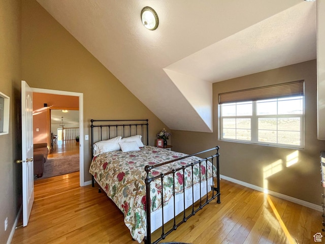 bedroom with vaulted ceiling, light wood-style flooring, and baseboards