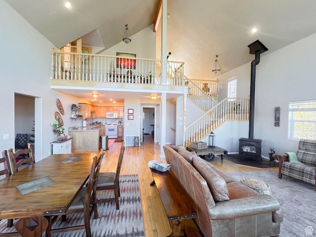 living room with high vaulted ceiling, a wood stove, light wood-style flooring, and stairs
