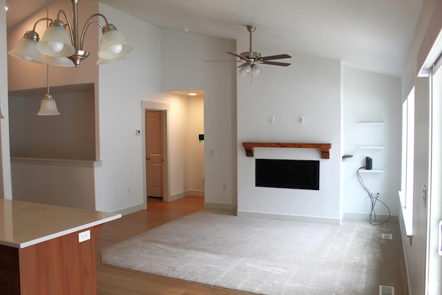 unfurnished living room featuring a fireplace, a ceiling fan, a chandelier, light wood-style flooring, and baseboards