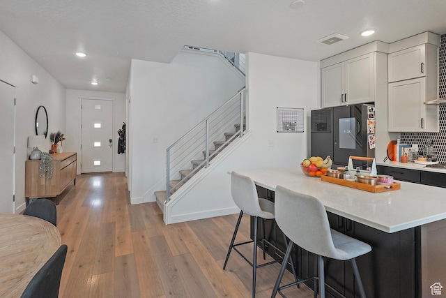 kitchen with refrigerator, a breakfast bar, white cabinets, light countertops, and light wood-type flooring