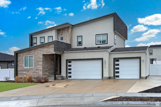 contemporary home featuring stone siding, driveway, and fence