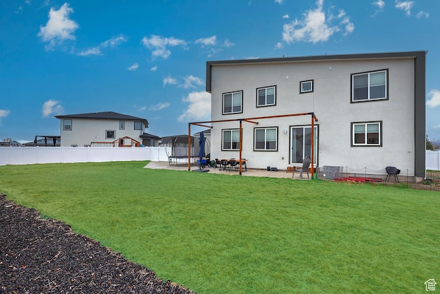 rear view of house with a trampoline, fence, a yard, a patio area, and stucco siding