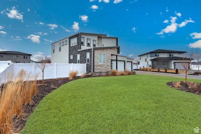back of house with stone siding, a lawn, an attached garage, and fence