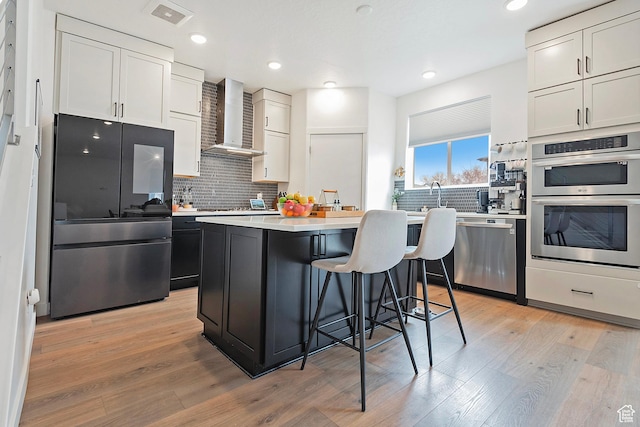 kitchen featuring stainless steel appliances, light countertops, light wood-style flooring, and wall chimney exhaust hood