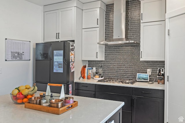 kitchen with decorative backsplash, wall chimney exhaust hood, freestanding refrigerator, light countertops, and stainless steel gas cooktop
