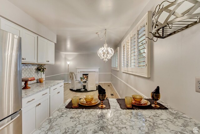 kitchen featuring a notable chandelier, white cabinets, freestanding refrigerator, light stone countertops, and tasteful backsplash