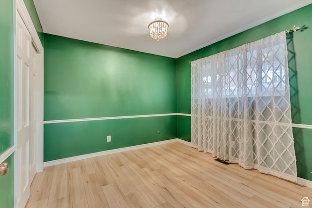 spare room featuring baseboards, visible vents, an inviting chandelier, and wood finished floors