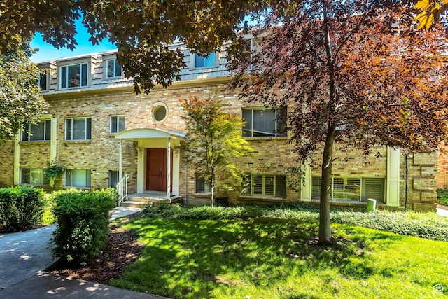 view of front facade featuring a front yard, mansard roof, and brick siding