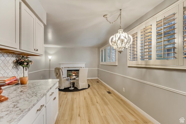 kitchen featuring a fireplace, white cabinets, baseboards, backsplash, and light wood finished floors