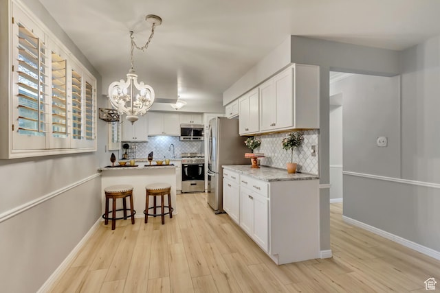 kitchen with light wood finished floors, backsplash, appliances with stainless steel finishes, a sink, and a peninsula
