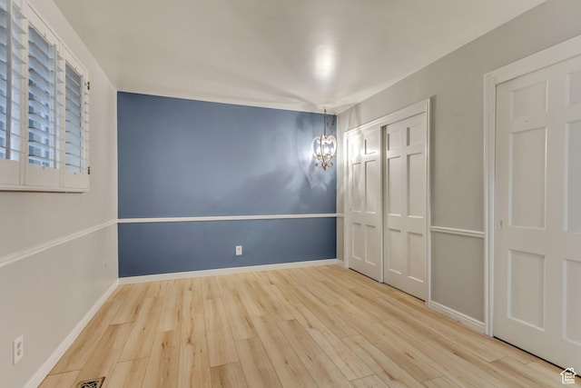 unfurnished bedroom featuring an inviting chandelier, a closet, baseboards, and wood finished floors
