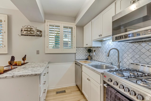 kitchen with light wood finished floors, decorative backsplash, appliances with stainless steel finishes, white cabinetry, and a sink