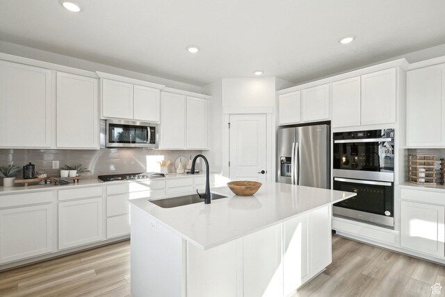 kitchen with a sink, light wood-style flooring, white cabinets, and stainless steel appliances